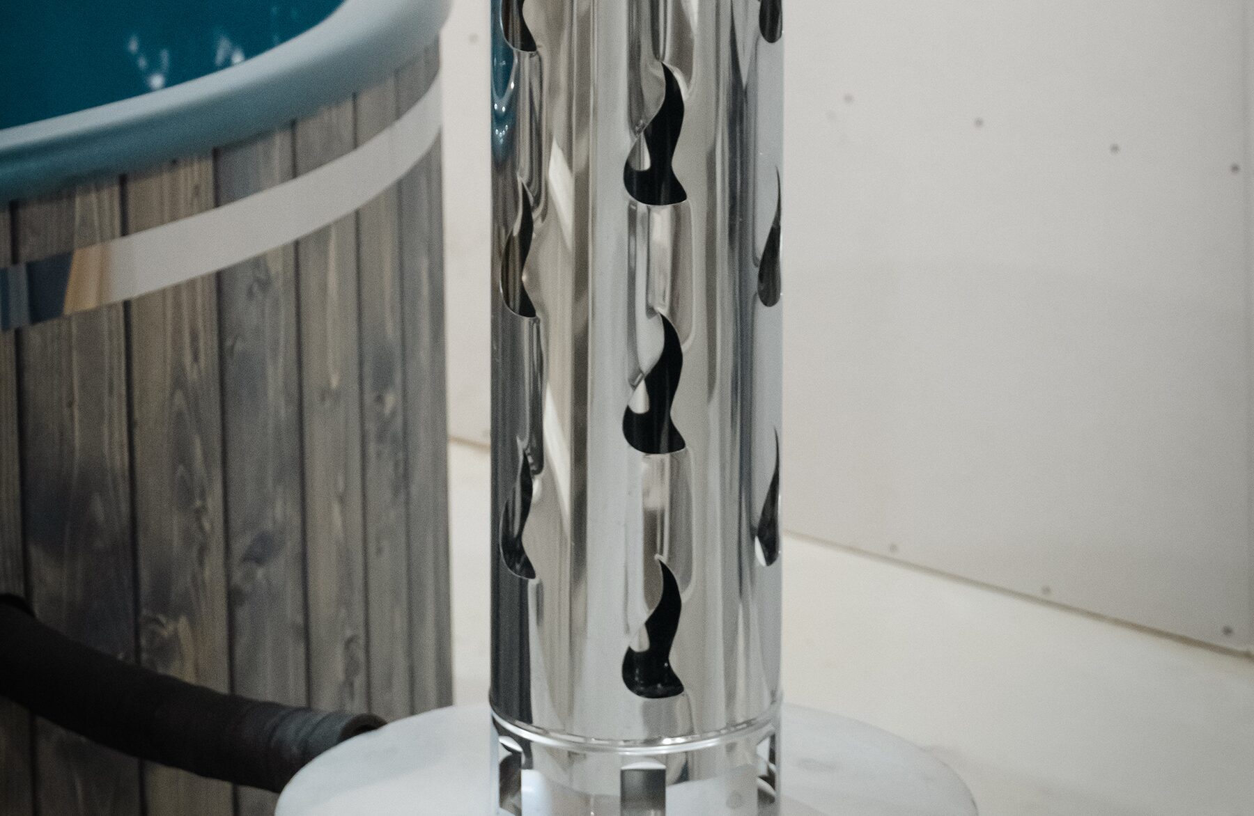 Makoya Spa hot tub DIANA set on a meadow featuring wooden cladding, a grey interior tub with integrated jets, wooden. Entry step and a external metal stove