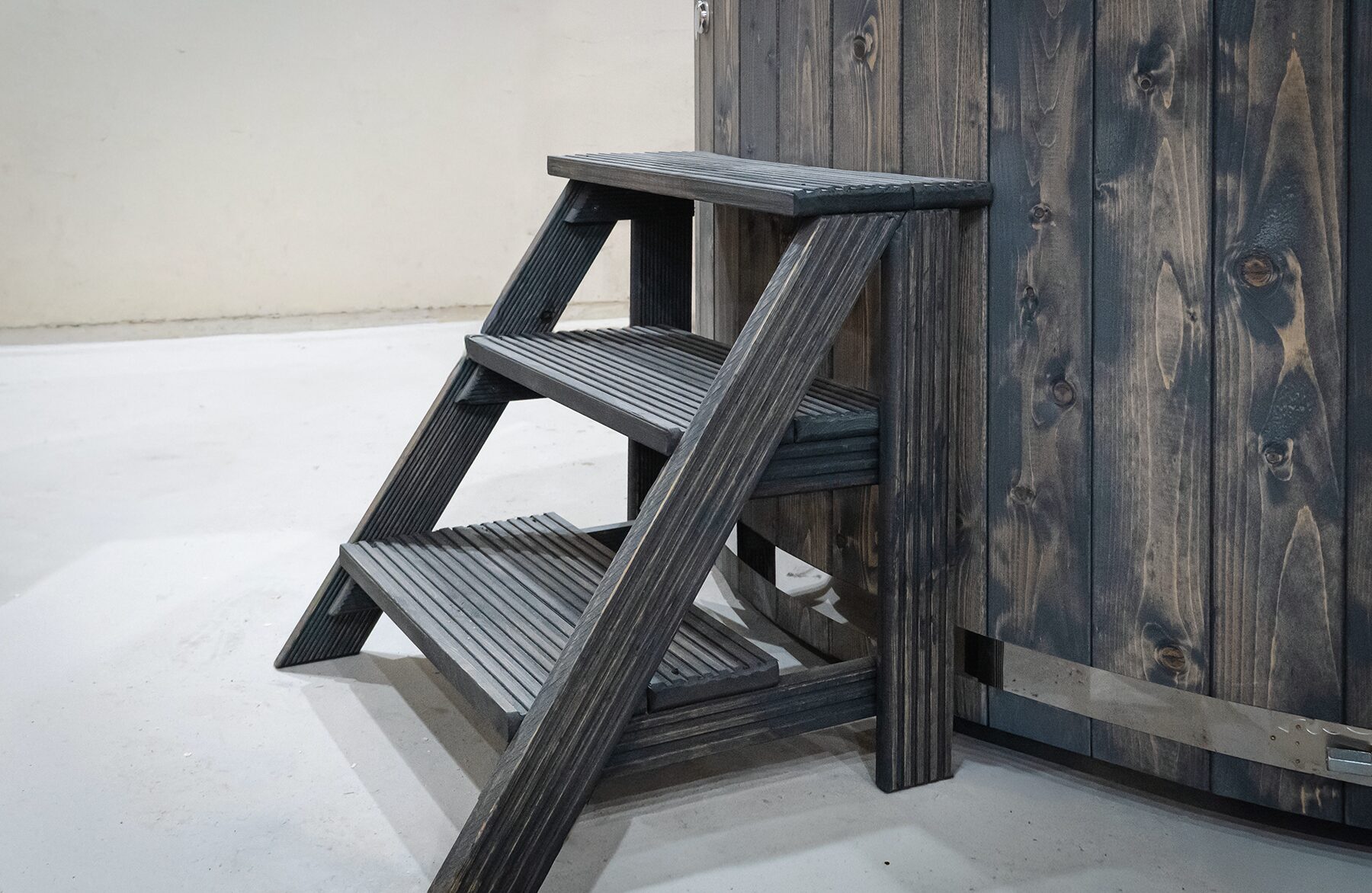 Wooden entry steps with three treads made of dark wood, positioned beside a Makoya Spa hot tub LUNA with wooden cladding.
