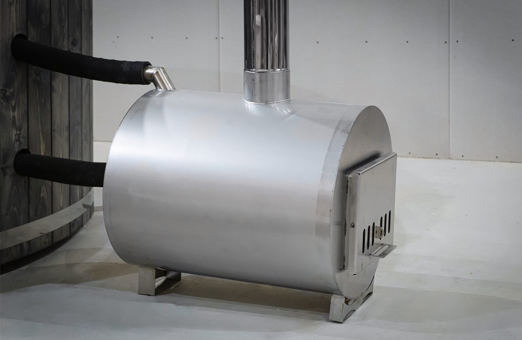 External metal stove of the Makoya Spa hot tub LUNA, featuring a chimney connection, isolated water pipes and a firebox door.