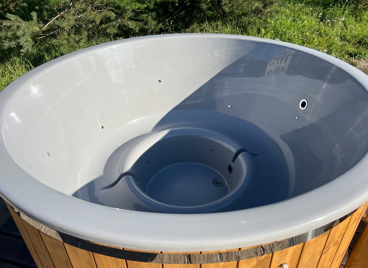 Close-up view of the grey interior tub of the Makoya Spa hot tub LUNA, featuring an ergonomic seating shape, integrated jets and a water drain, surrounded by wooden cladding in an outdoor setting. 