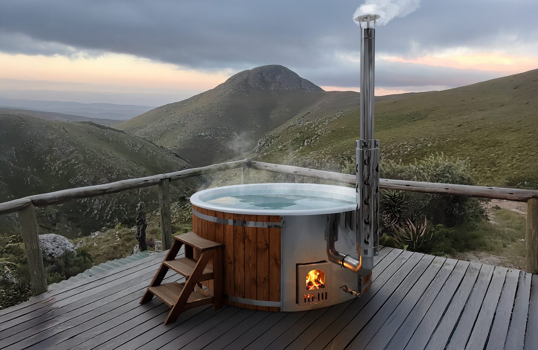 Hot tub SOPHIA by Makoya Spa, made of wood, on a terrace, overlooking green mountains under a cloudy sky.