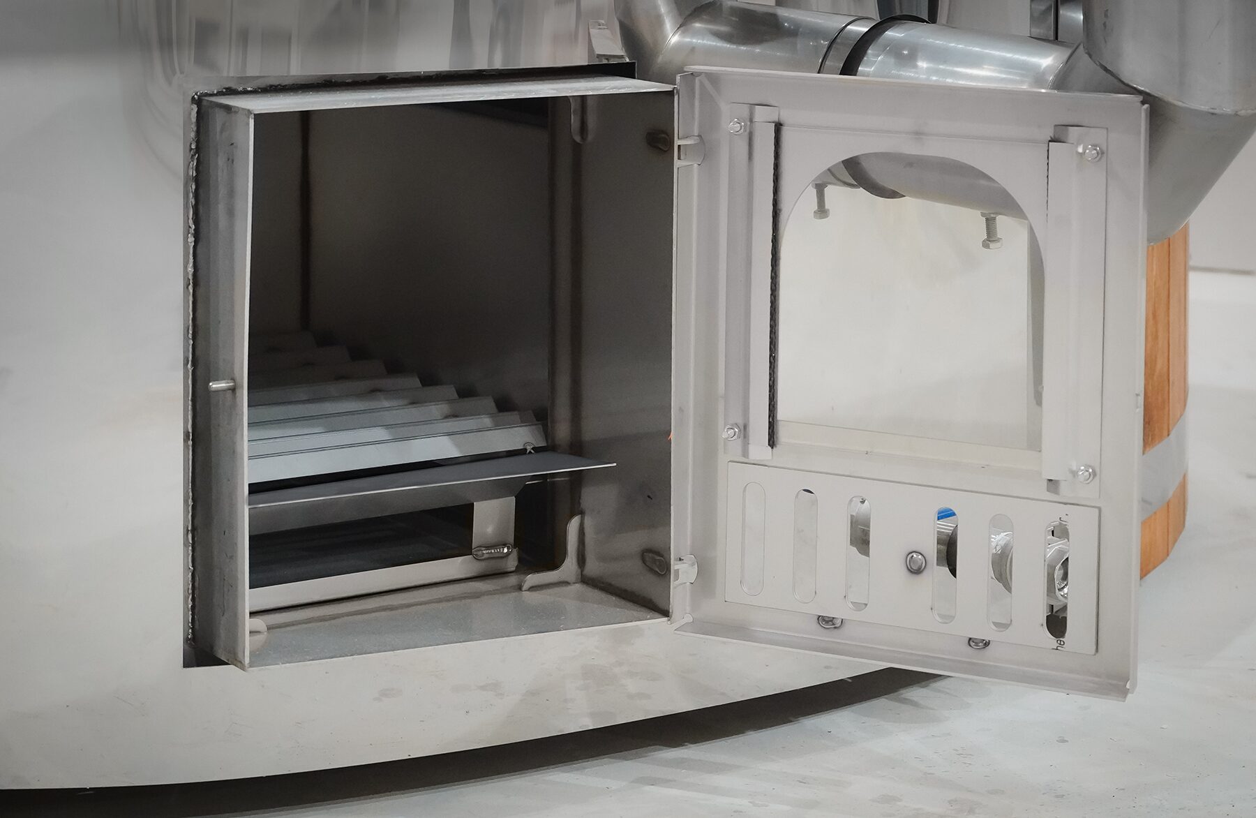 Open metal stove of a Makoya Spa hot tub SOPHIA, showing the firebox interior, combustion chamber and air intake, including the internal pipe connection.