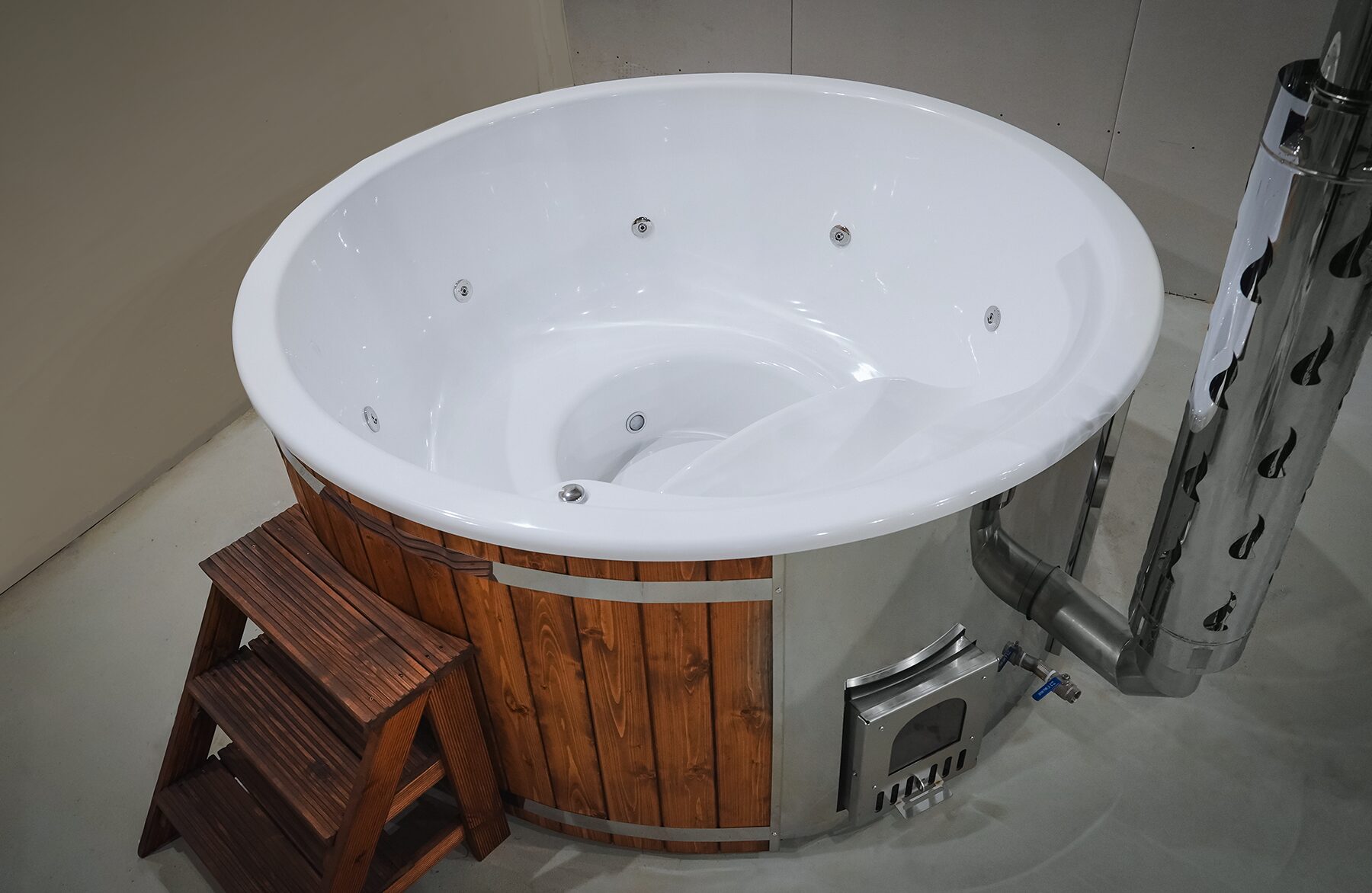 Makoya Spa hot tub SOPHIA with a white interior tub and integrated jets, wooden cladding, a metal stove with chimney connection and wooden entry steps.