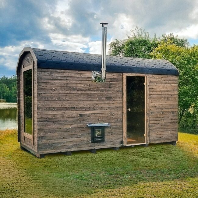 Makoya Spa sauna CERES set on a meadow, surrounded by bushes and trees, with a lake and blue sky visible in the background.