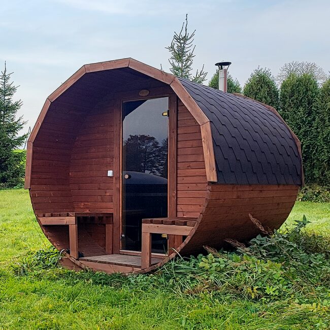Barrel sauna JUNO by Makoya Spa, on a meadow with trees and blue sky in the background.