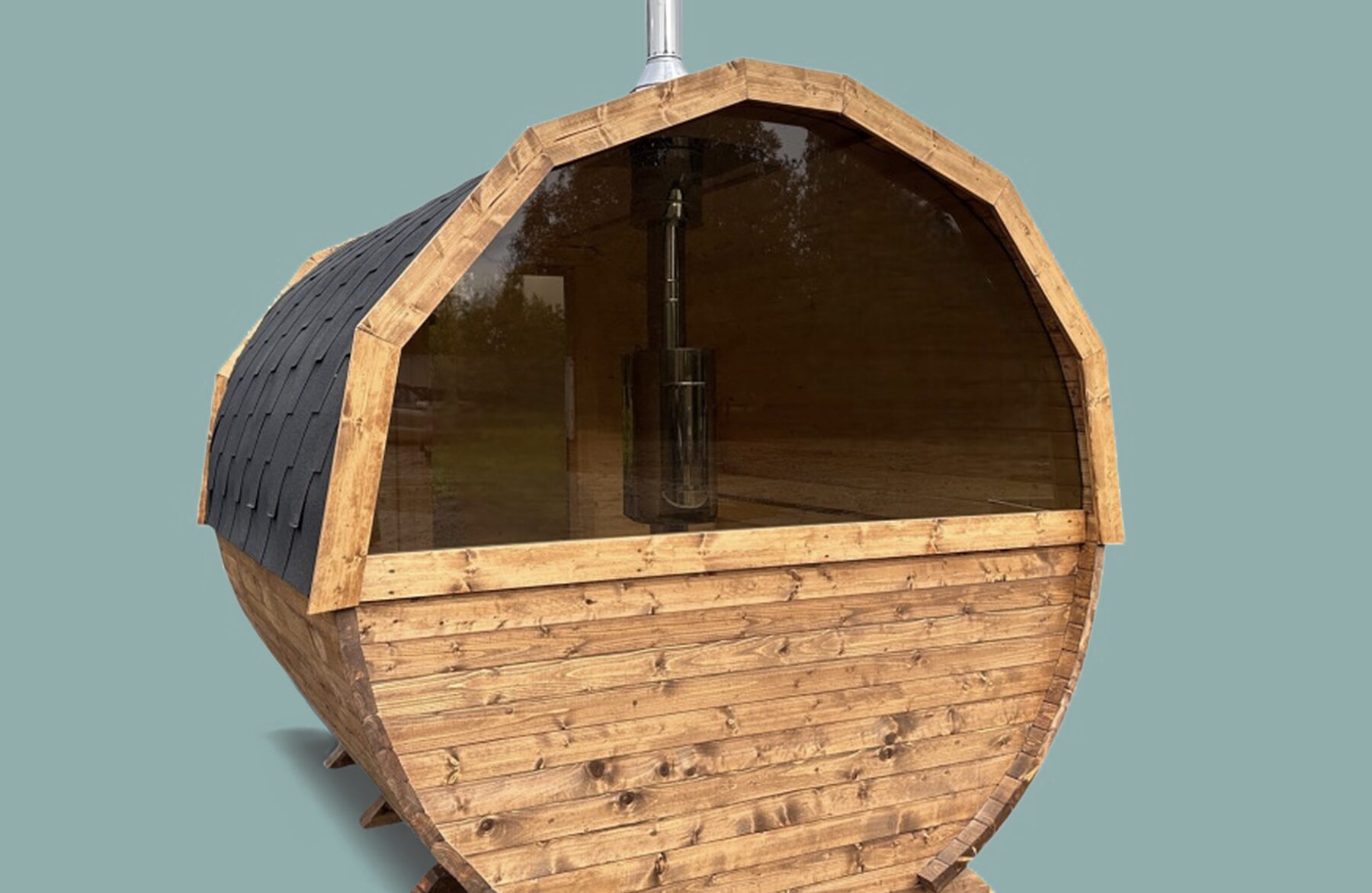 Front view of the Makoya Spa sauna JUNO in a round barrel design with natural wooden cladding, a large panoramic glass window, a black shingle roof and a chimney, against a neutral background.