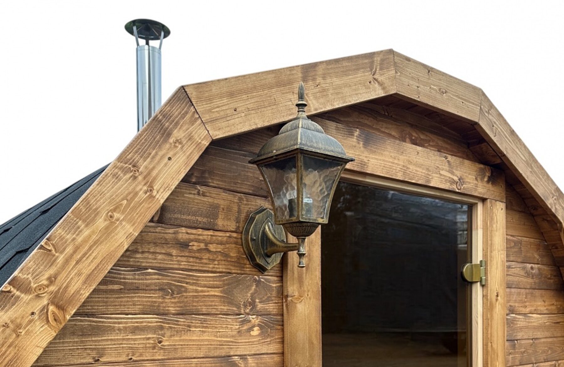 Close-up view of the Makoya Spa barrel sauna JUNO featuring rustikal wooden cladding, a glass door a decorative exterior lamp and a visible chimney, against a light background.