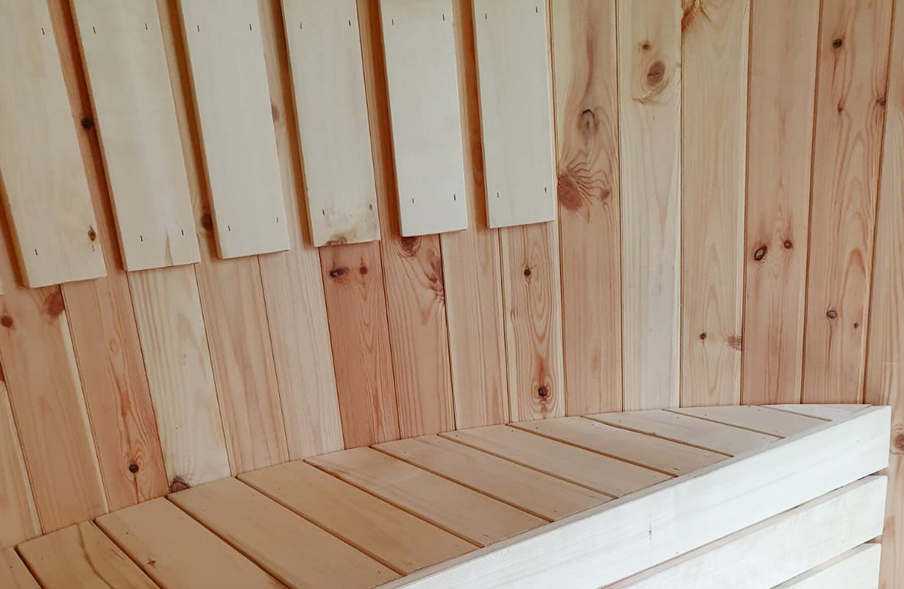 Detailed view of the sauna VESTA by Makoya Spa, featuring a smooth, light wooden surface, neatly crafted wooden slats and visible natural grain on both the wall and the seating area.