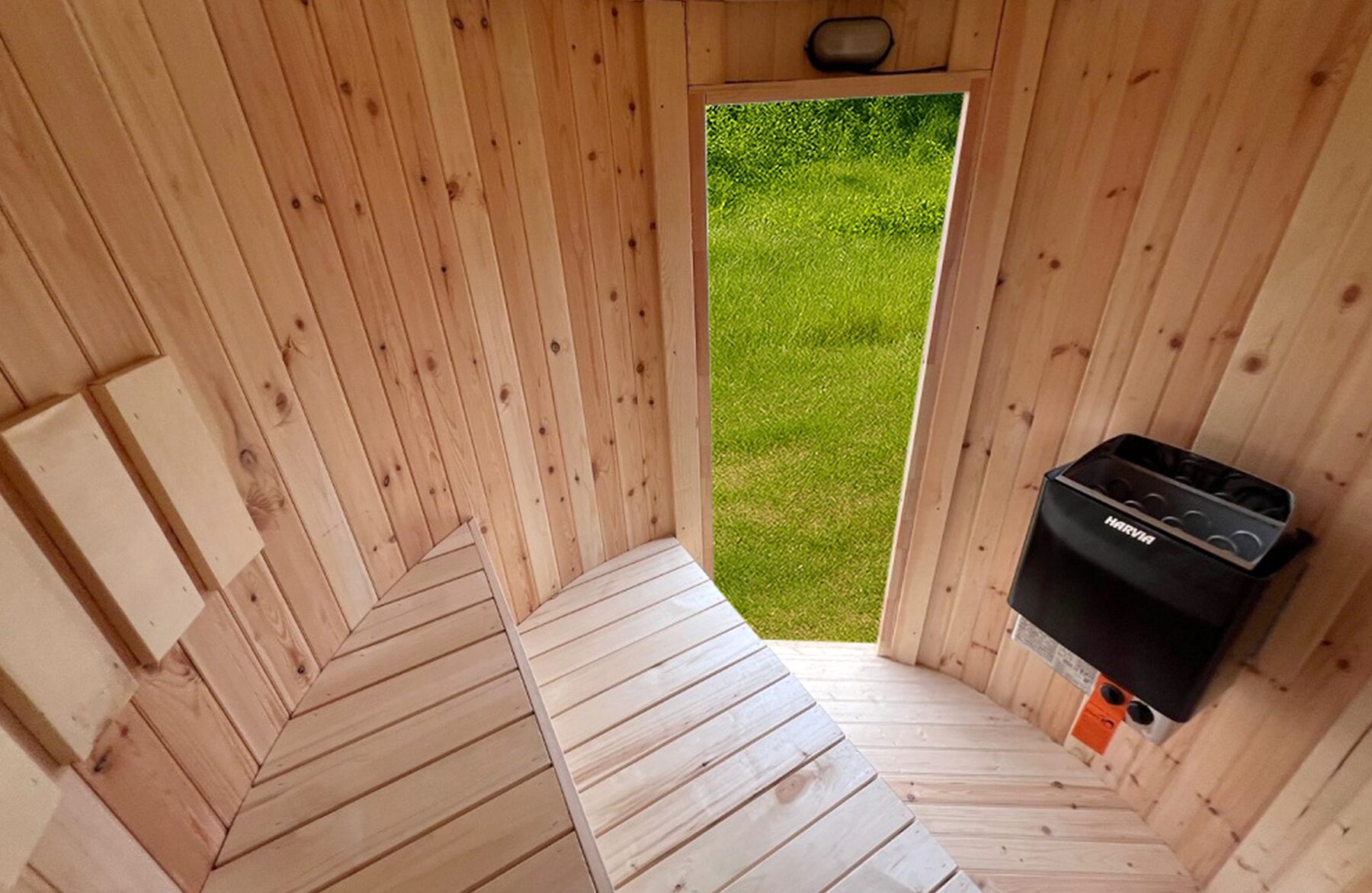 Interior view of the sauna VESTA by Makoya Spa featuring light wooden cladding, ergonomically arranged wooden benches, a wooden floor, an open door with a view of green surroundings and a black sauna heater mounted on the wall.