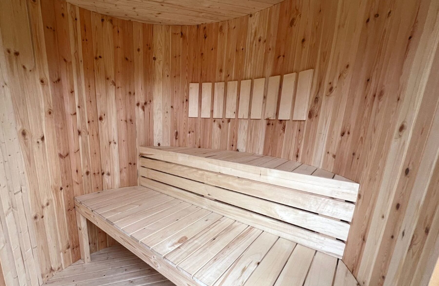 Interior view of the sauna VESTA by Makoya Spa featuring light wooden cladding, two-tier wooden benches, ergonomic seating and reclining surfaces and a calm, natural wood design inside the sauna room.