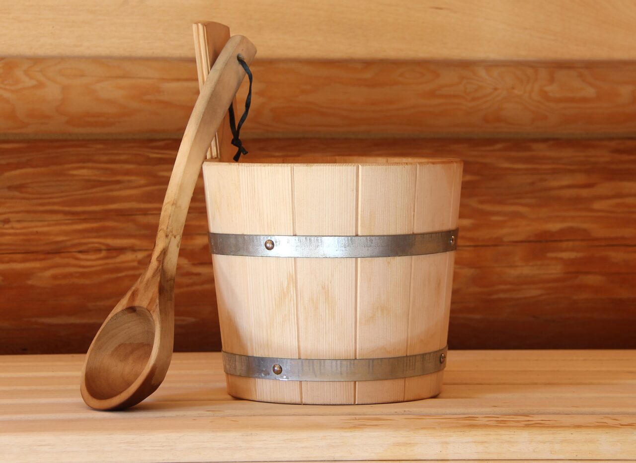Wooden sauna bucket including spoon in front of a wooden background
