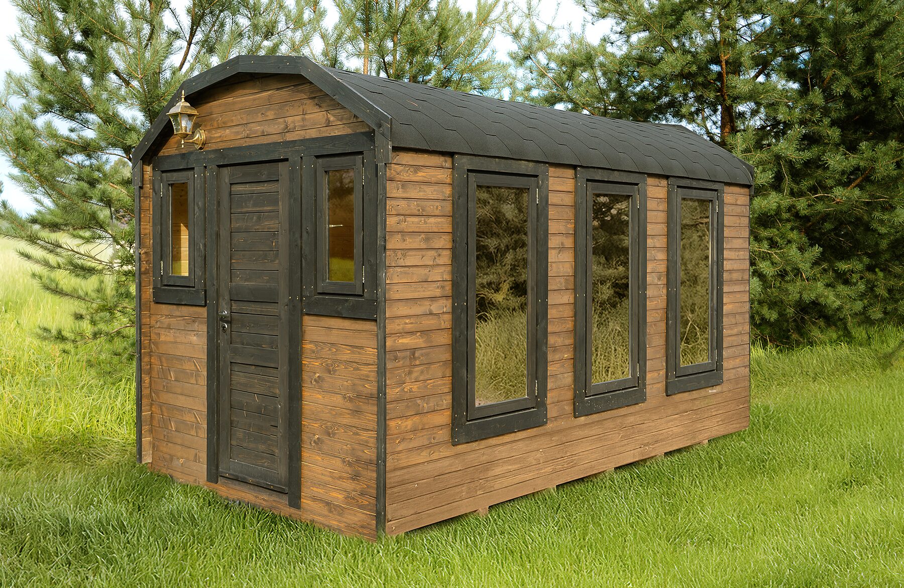 Exterior view of a Makoya Spa tiny house CERES with dark wooden framing and warm wood cladding. The compact home is set on a green meadow surrounded by pine trees. Large windows provide plenty of natural light, while the dark, gently sloped roof adds a modern, nature-inspired appearance.