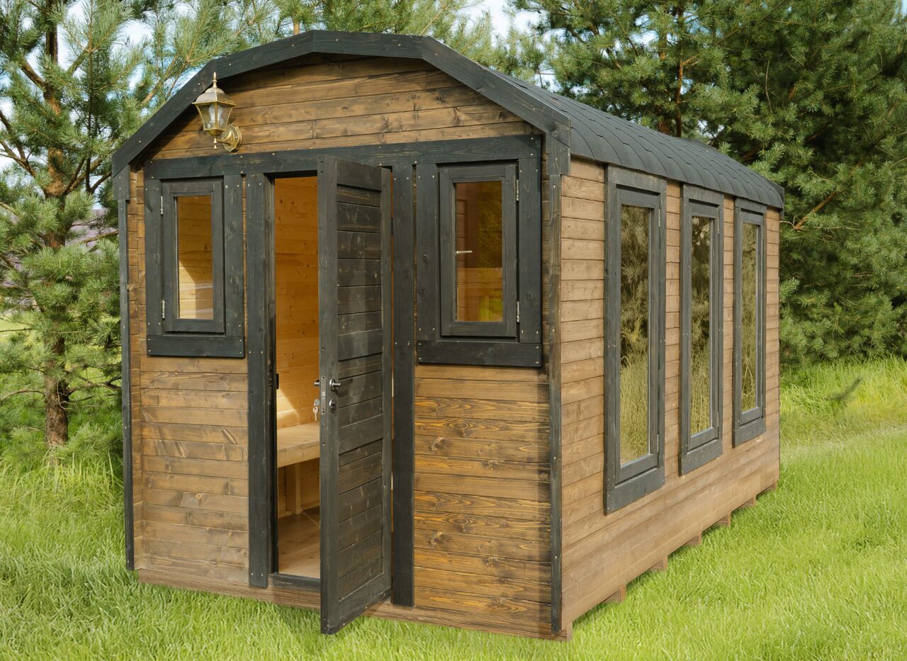 Exterior view of a Makoya Spa tiny house CERES with brown wooden cladding and black-framed windows and door. The entrance door is open, revealing the bright wooden interior. The tiny house is set on a green lawn and surrounded by trees, creating a calm, nature-oriented setting.