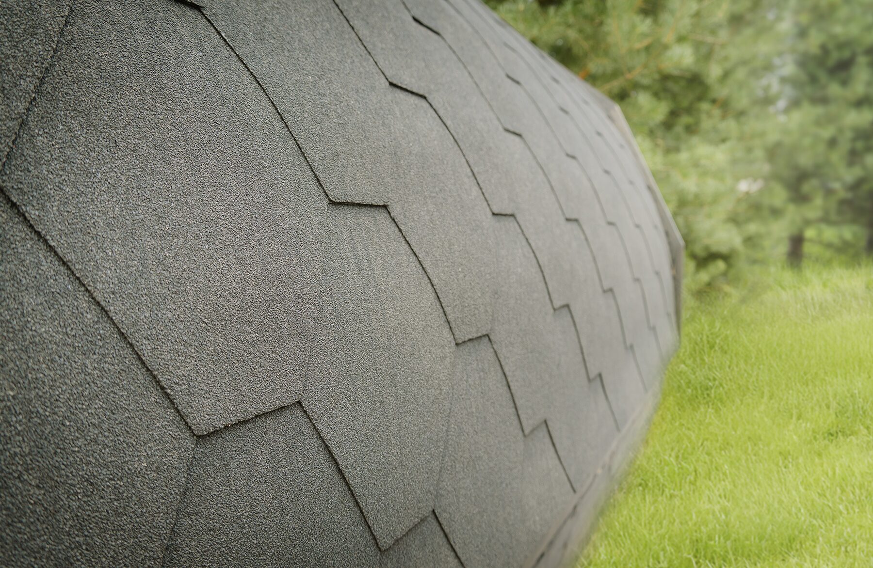 Close-up view of the curved roof of the Makoya Spa tiny house JUNO with grey roof shingles, highlighting the high-quality texture and finish, set against a green meadow and natural surroundings.