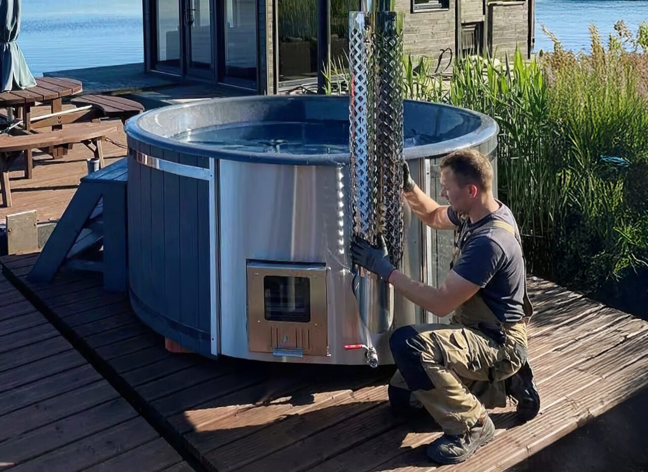 A technician installs a stainless steel oven on a hot tub by Makoya Spa on a wooden deck by water.