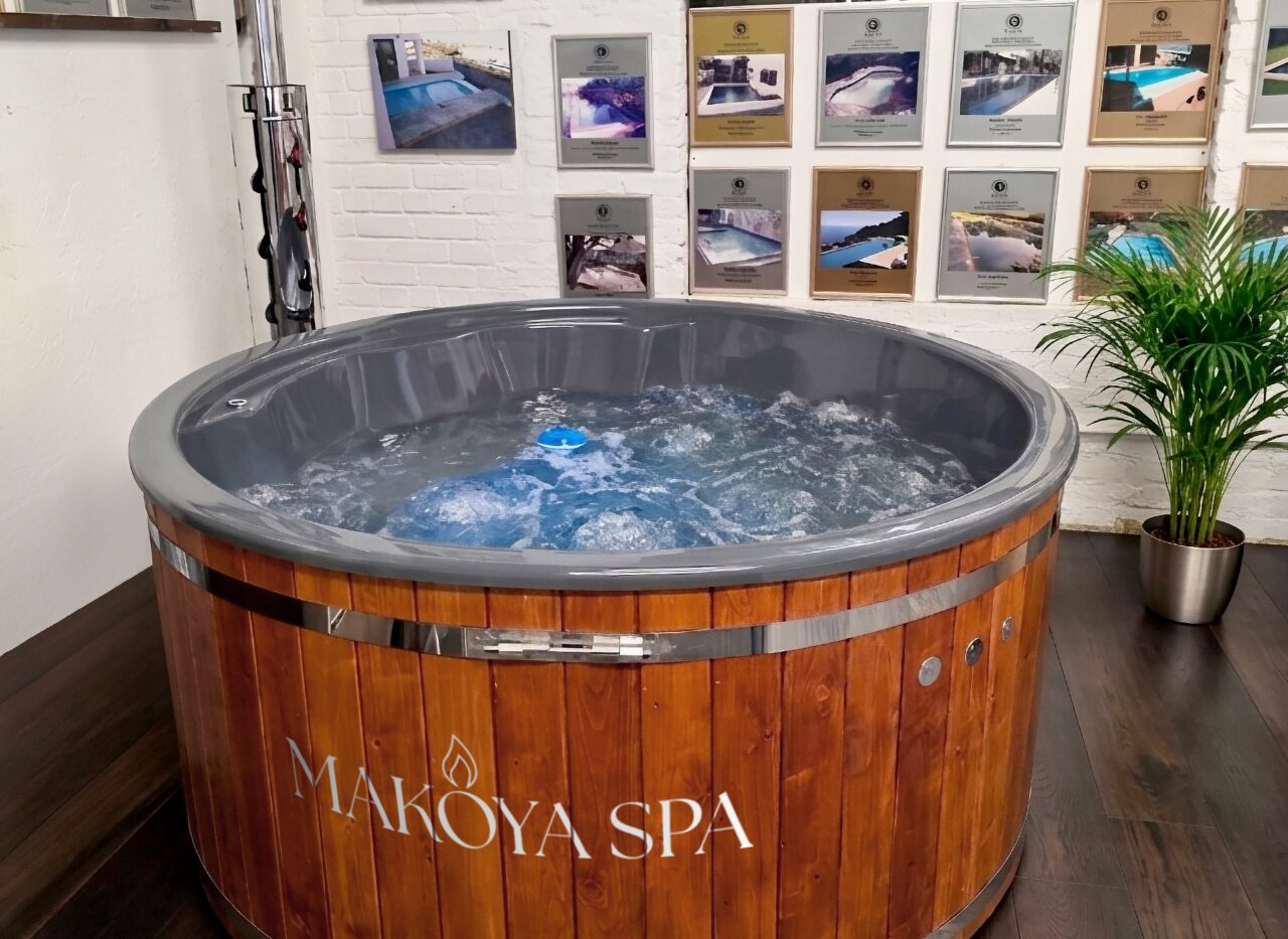 Close-up view of a Makoya Spa hot tub featuring a grey interior tub with integrated massage jets and wooden cladding in an indoor setting.