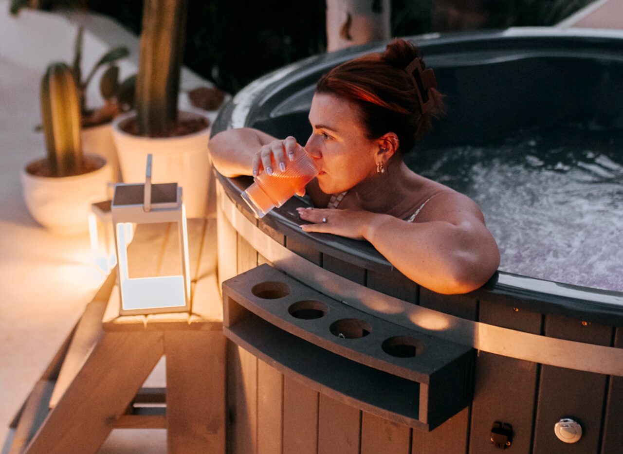Person relaxing in a Makoya Spa hot tub SOPHIA, drinking from a glass.